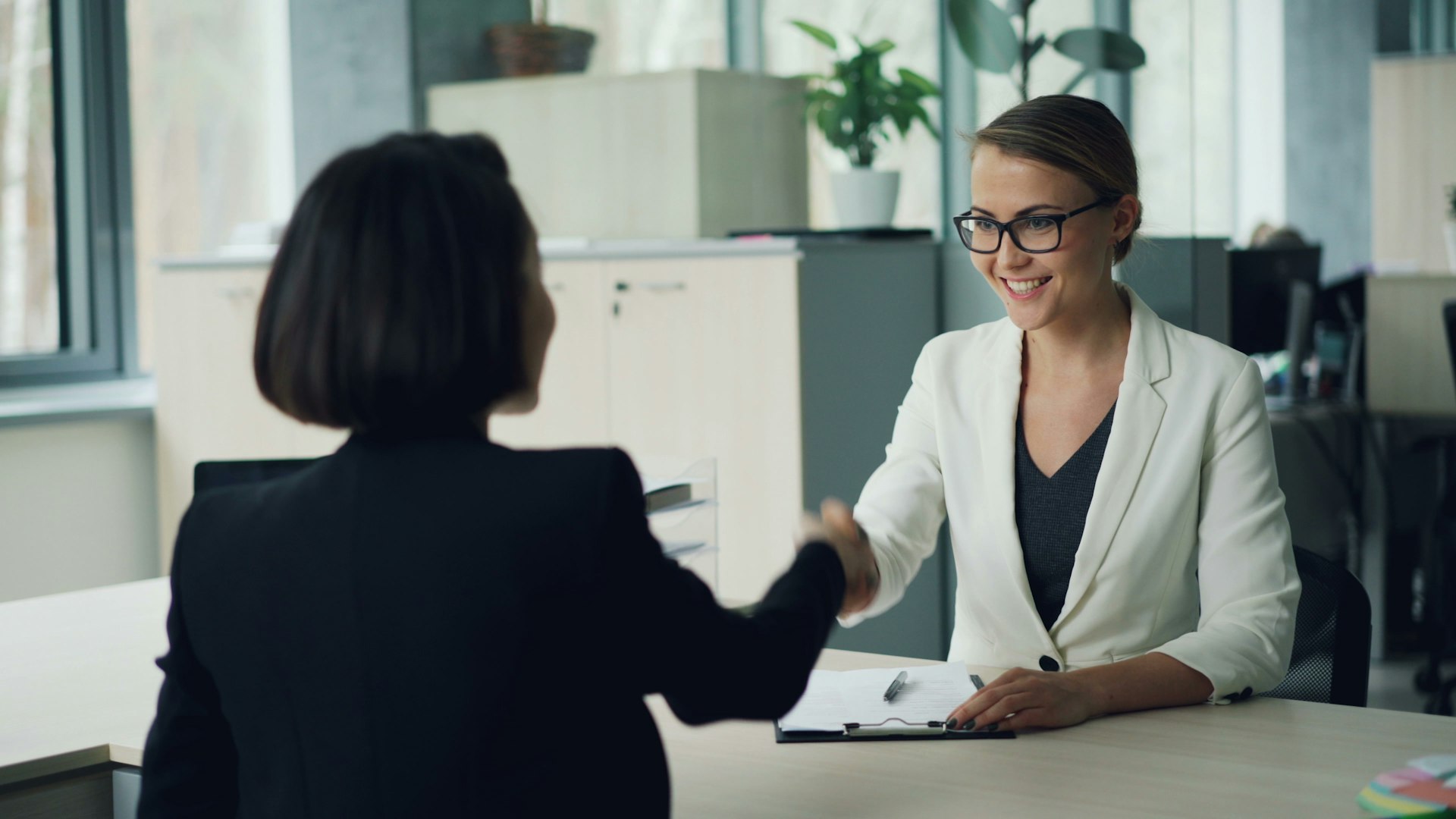 Two women shaking hands across a desk